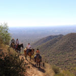 A landscape view of horseback riders on the Pass Hiking Trail, in Usery Park with the mountains and Mesa, Arizona in the background. Phoenix area hiking trails. Moderate hiking trails. Copyright azutopia.com. No use without permission.