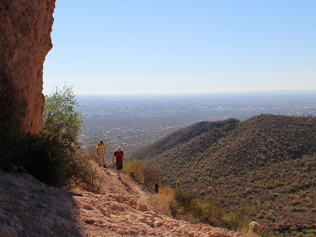 A landscape view of hikers at the pass of Usery Park' Pass Mountain, with the town of Mesa below. From the Pass Mountain Hiking Trail Loop in Mesa, Arizona. Phoenix area hiking trails, Moderate hiking trails. Copyright azutopia. No use without permission. 