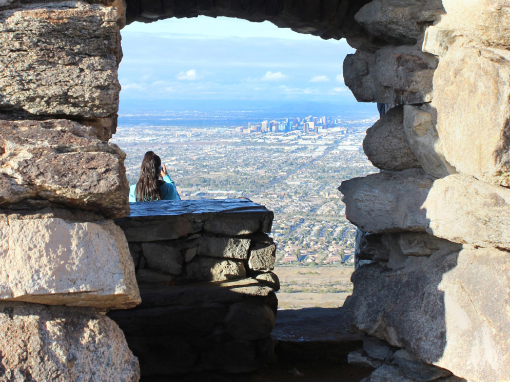 A hiker looking over downtown Phoenix, from Dobbins Lookout, at the top of the Holbert Hiking Trail, in South Mountain Park, Phoenix, Arizona. Stone structure, View, Moderate Hiking Trails, Phoenix Area Hiking Trails. copyright azutopia.com. No use without permission.