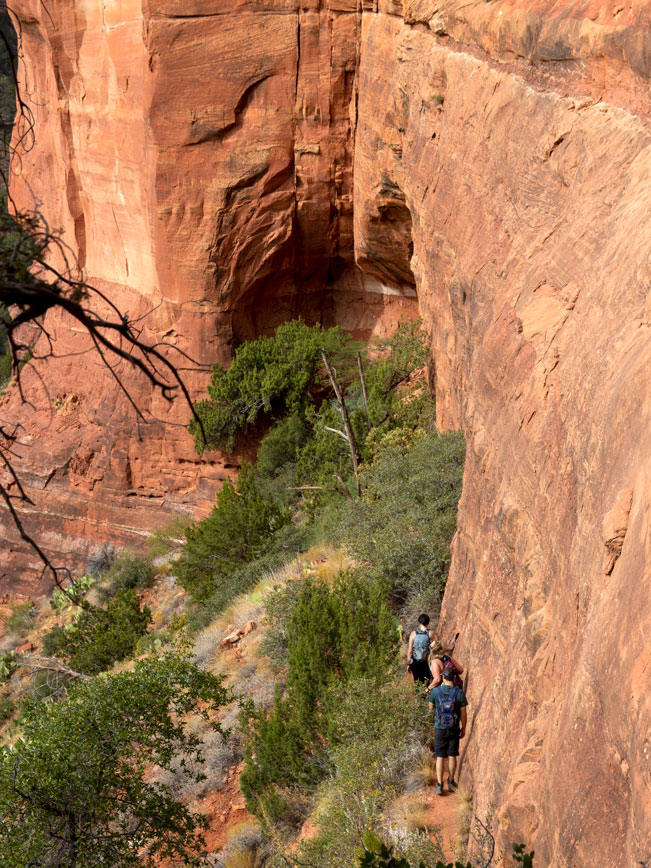 Landscape view of hikers walking alongside of arch; in Fay Canyon, Sedona; Arizona. Red n Rock formations and shrubs. Narrow walkway. Difficult Hiking Trails; Northern Arizona Hiking Trails. . Copyright azutopia.com. No use without permission.