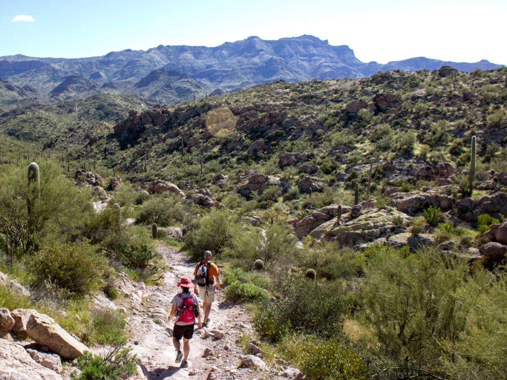 Landscape view, Hikers descending rocky trail, Tall Mountains in the Background, Saguaros, Palo Verdes and Scrub in front, Superstition Mountains, Black Mesa Hiking Trail Loop, Grand Enchantment Hiking Trail, Second Water Hiking Trail, Apache Junction, Arizona, Copyright azutopia.com, No use without permission